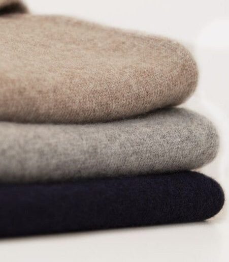 Tre mjukt vikta tröjor i beige, grått och mörkblått