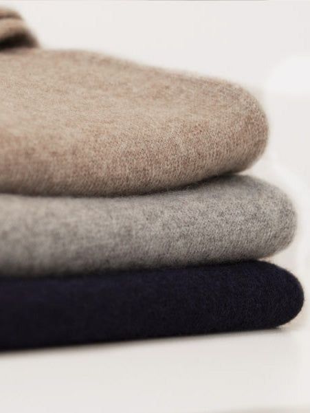 Tre mjukt vikta tröjor i beige, grått och mörkblått